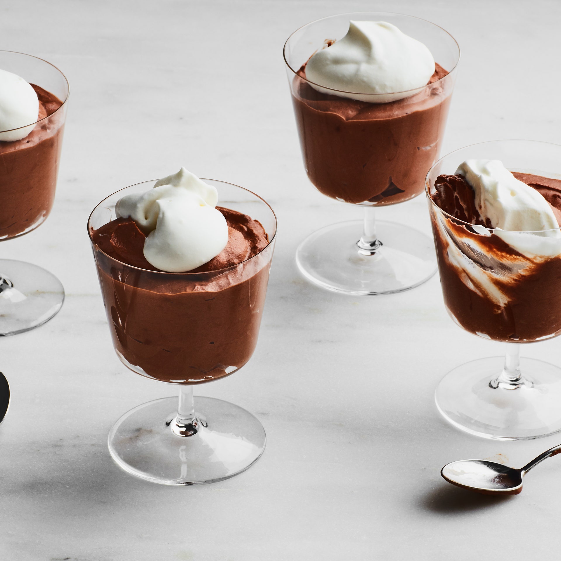 Chocolate mousse in dessert glasses with whipped cream on top and spoons on the side.