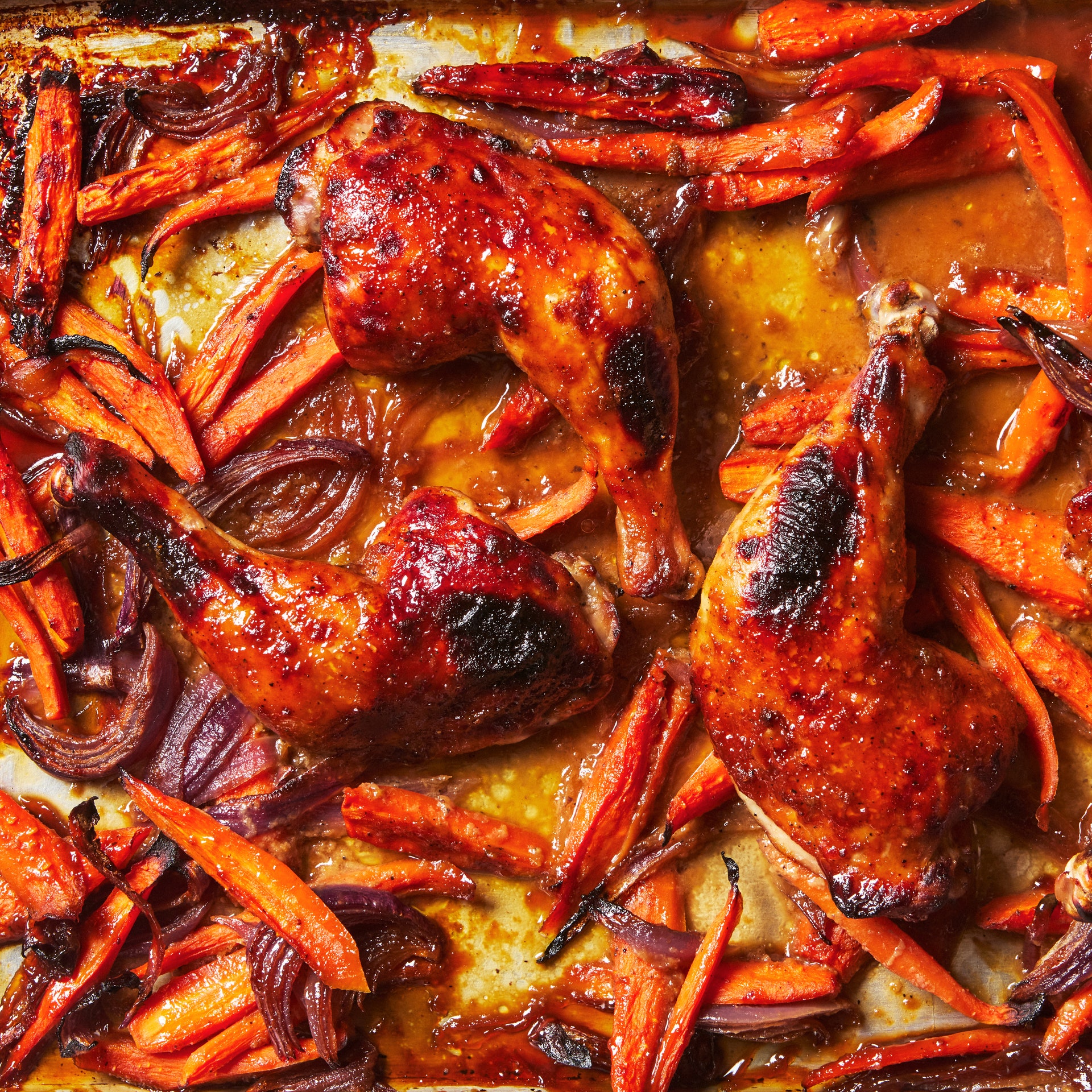 Chicken legs on a sheet pan with an apricot jam sauce roasted onions and carrots.